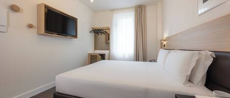 A modern hotel room with a large bed, a television mounted on the wall, a bedside table, and a wardrobe with a mirror.
