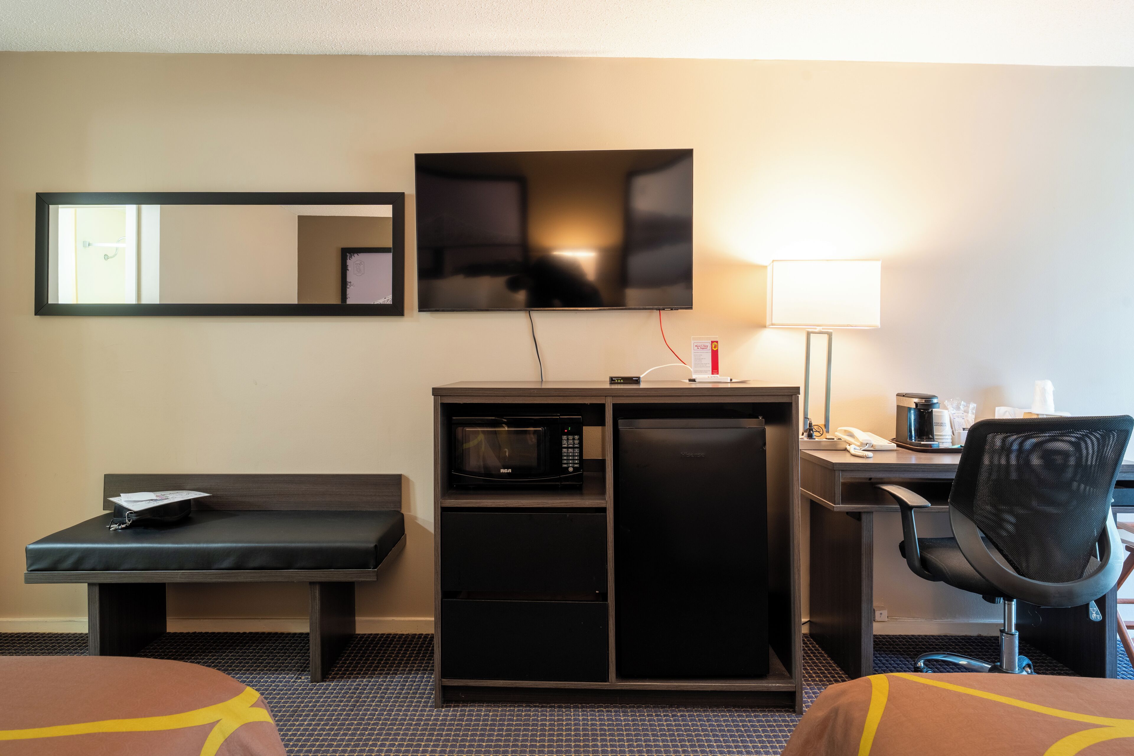 Habitación de hotel con cama, escritorio con computadora, microondas, silla y mueble pequeño.