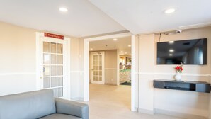 Un hall de hotel con un sofá gris, un mostrador de recepción, un televisor de pantalla plana montado en la pared y un cartel que indica un spa.