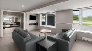 A modern living room with grey sofas, a small round table, and a TV mounted on the wall. - Super 8 by Wyndham Gananoque/Country Squire Resort (Gananoque)