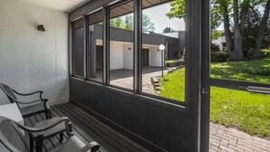 Un porche cubierto con una mesa y sillas, vista de una casa con garaje y un jardín césped.