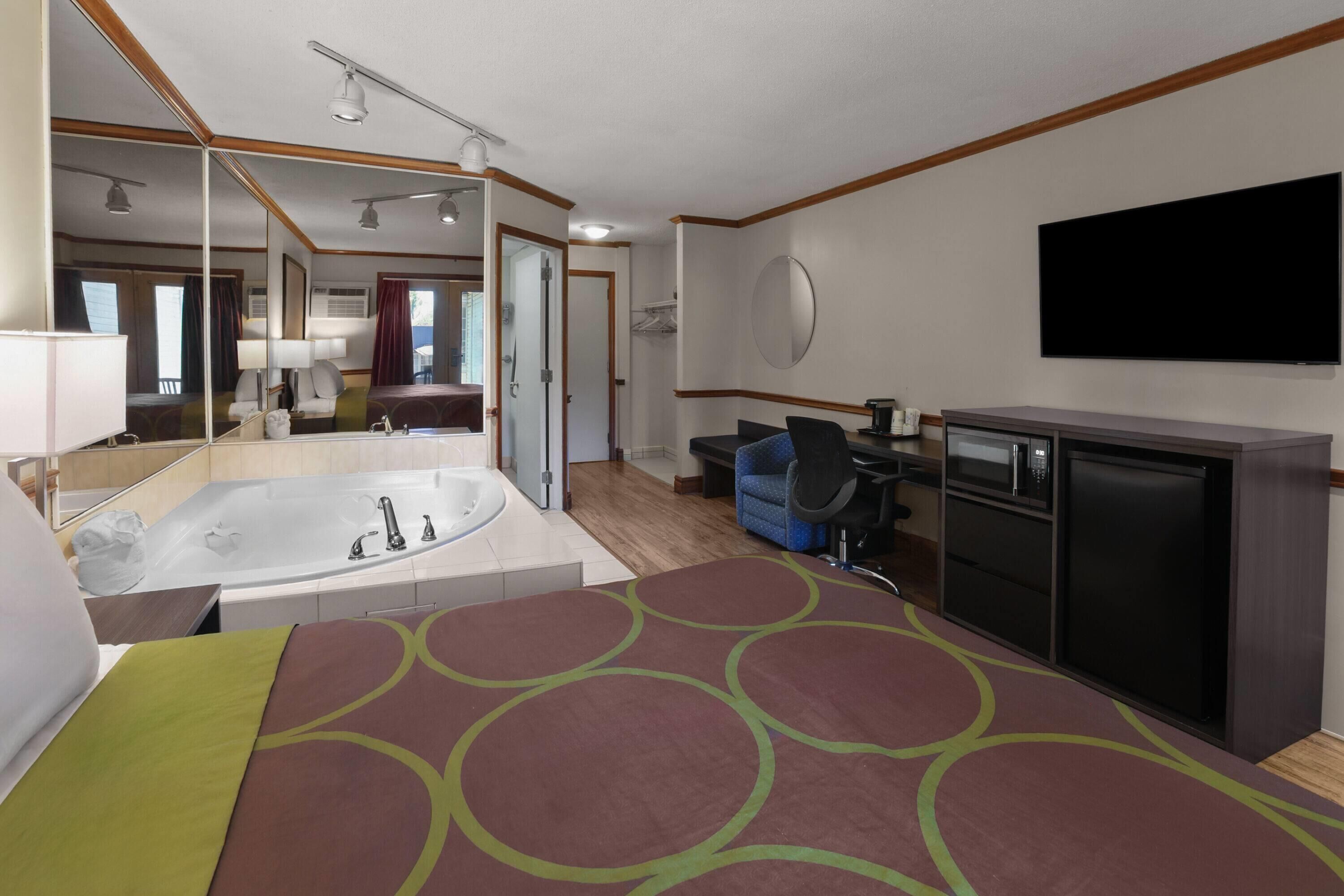A hotel room with a large bed, a bathroom with a bathtub, a desk with a chair, a television, and a wardrobe.