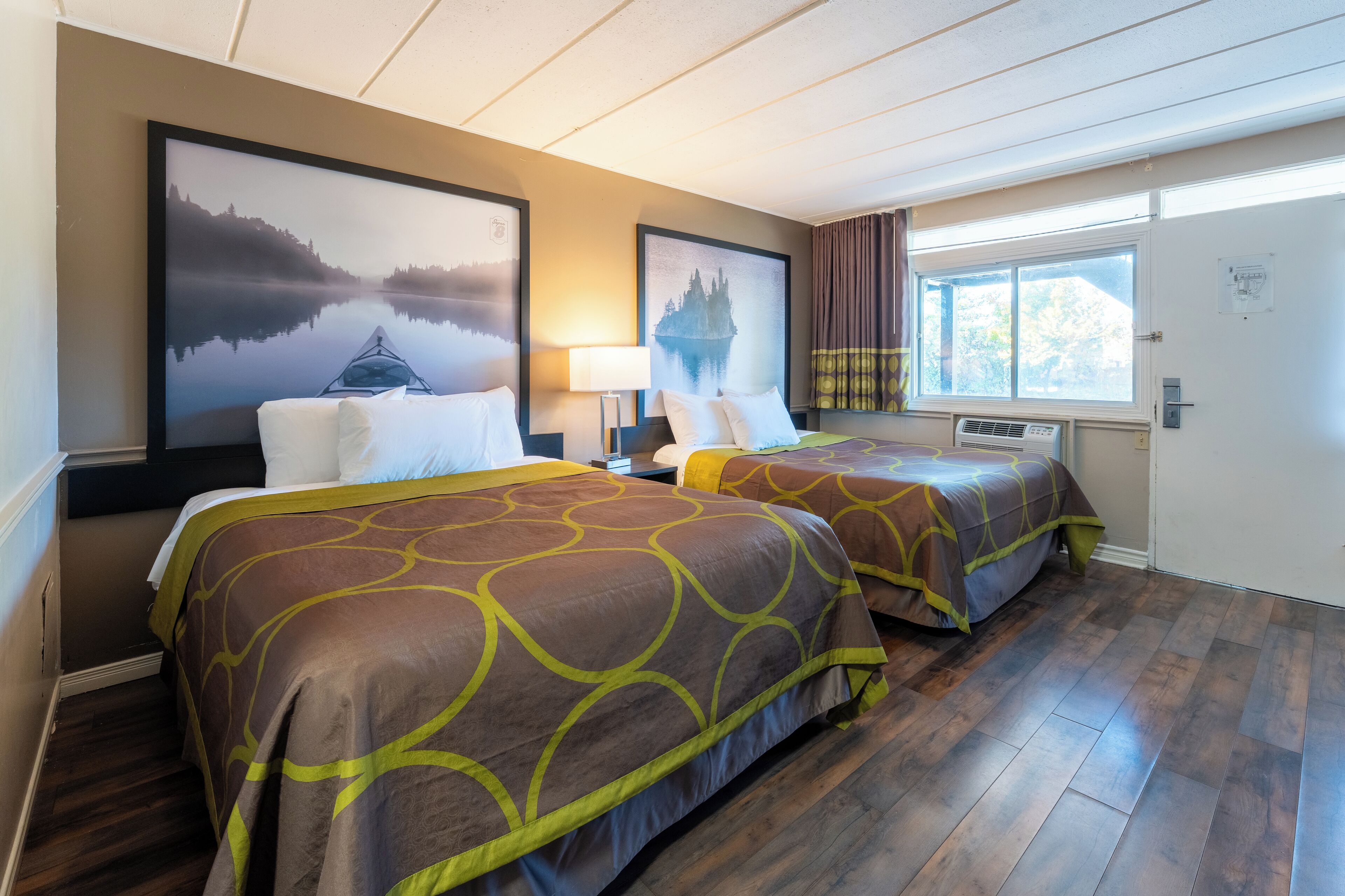 A hotel room with two beds, a large window, and artwork on the walls.
