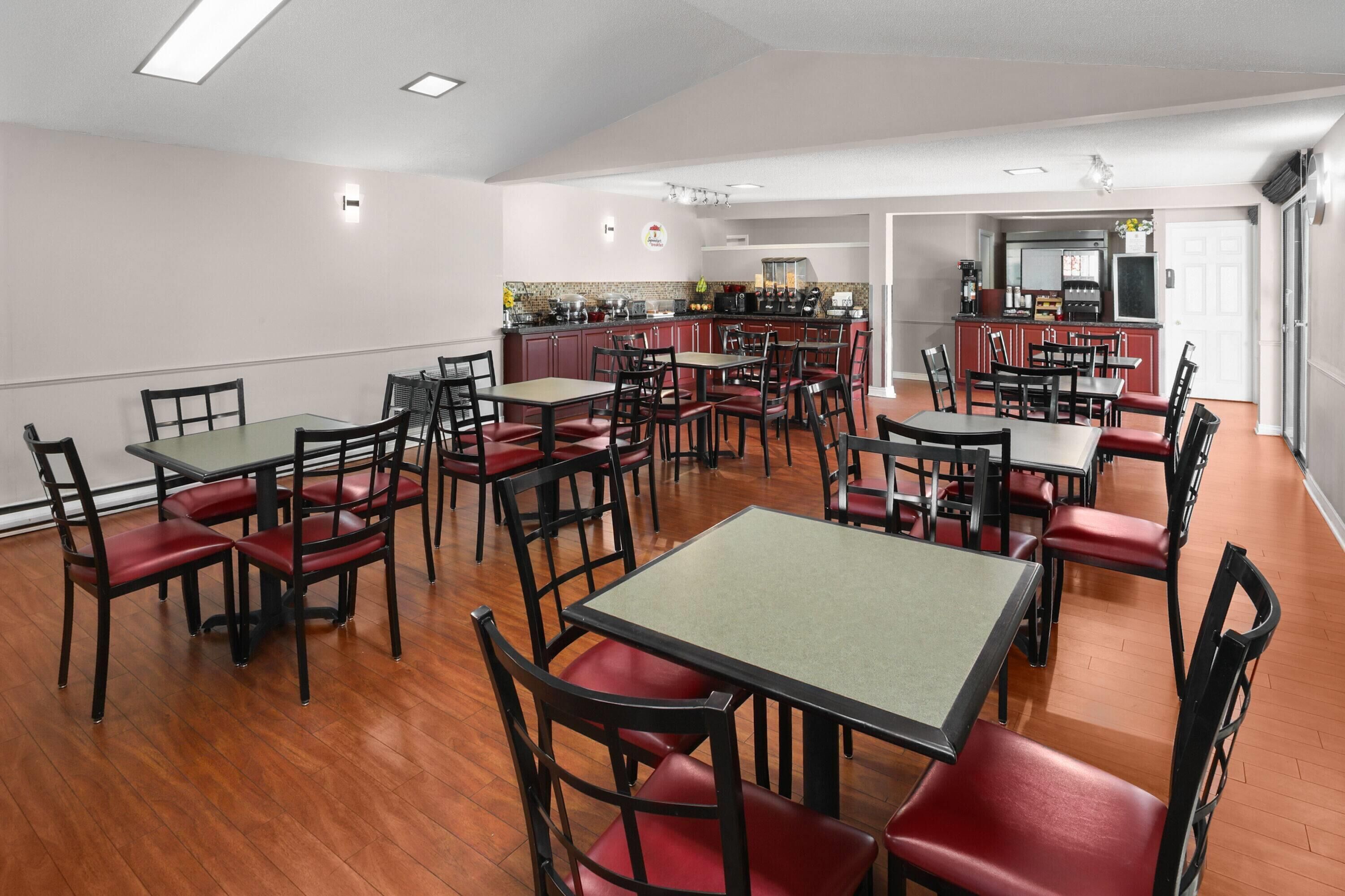 Comedor con varias mesas y sillas, cocina al fondo y una puerta que da a otra habitación.