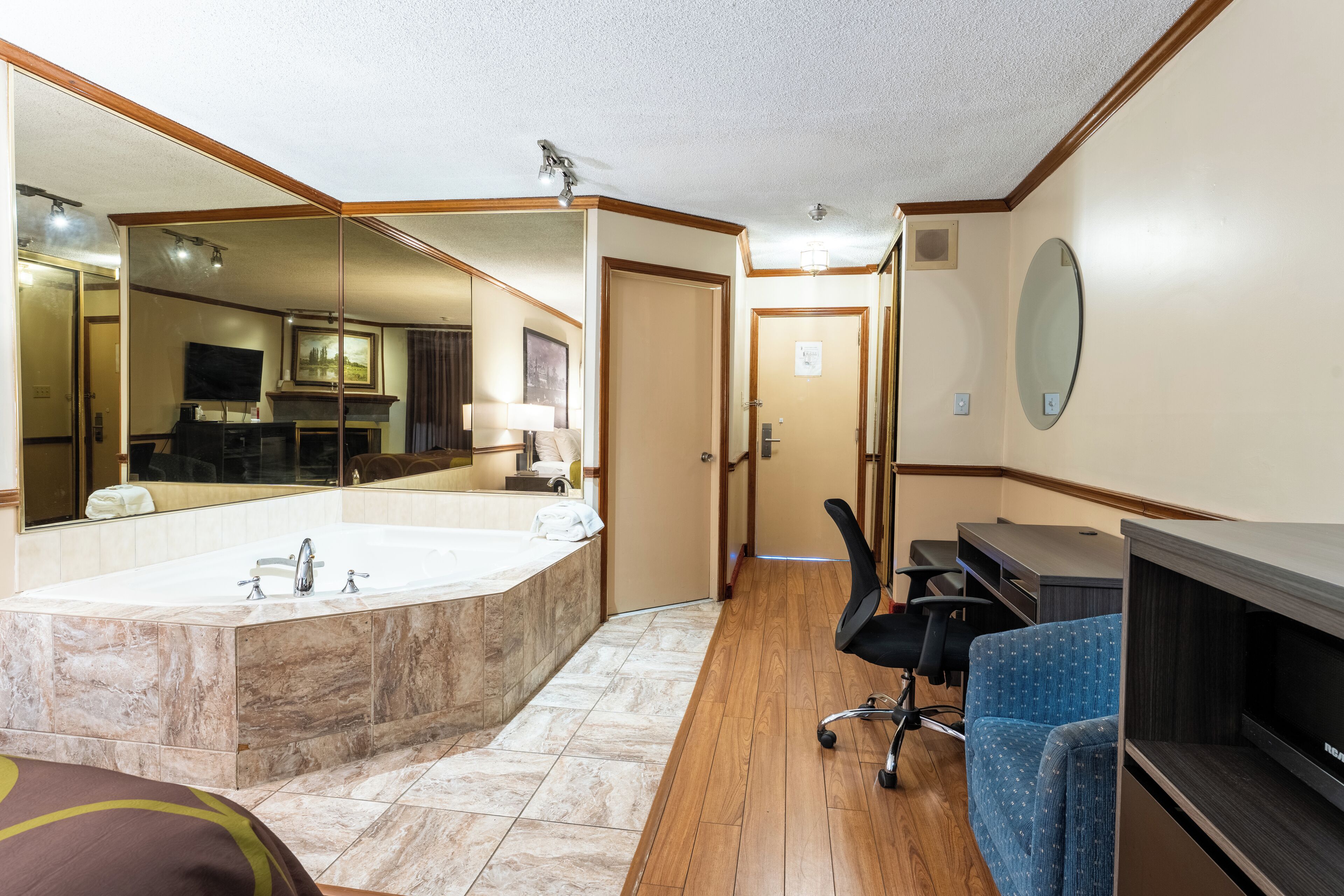 A hotel bathroom with a large mirror, a bathtub, a vanity with a mirror, and a seating area with chairs.