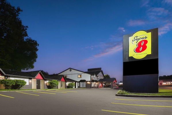 Un hotel Super 8 con un cartel grande, un estacionamiento y un edificio de techo rojo.