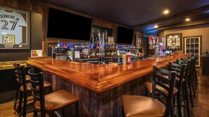 Una zona de bar con mostrador de madera, varios taburetes y una variedad de botellas y vasos.
