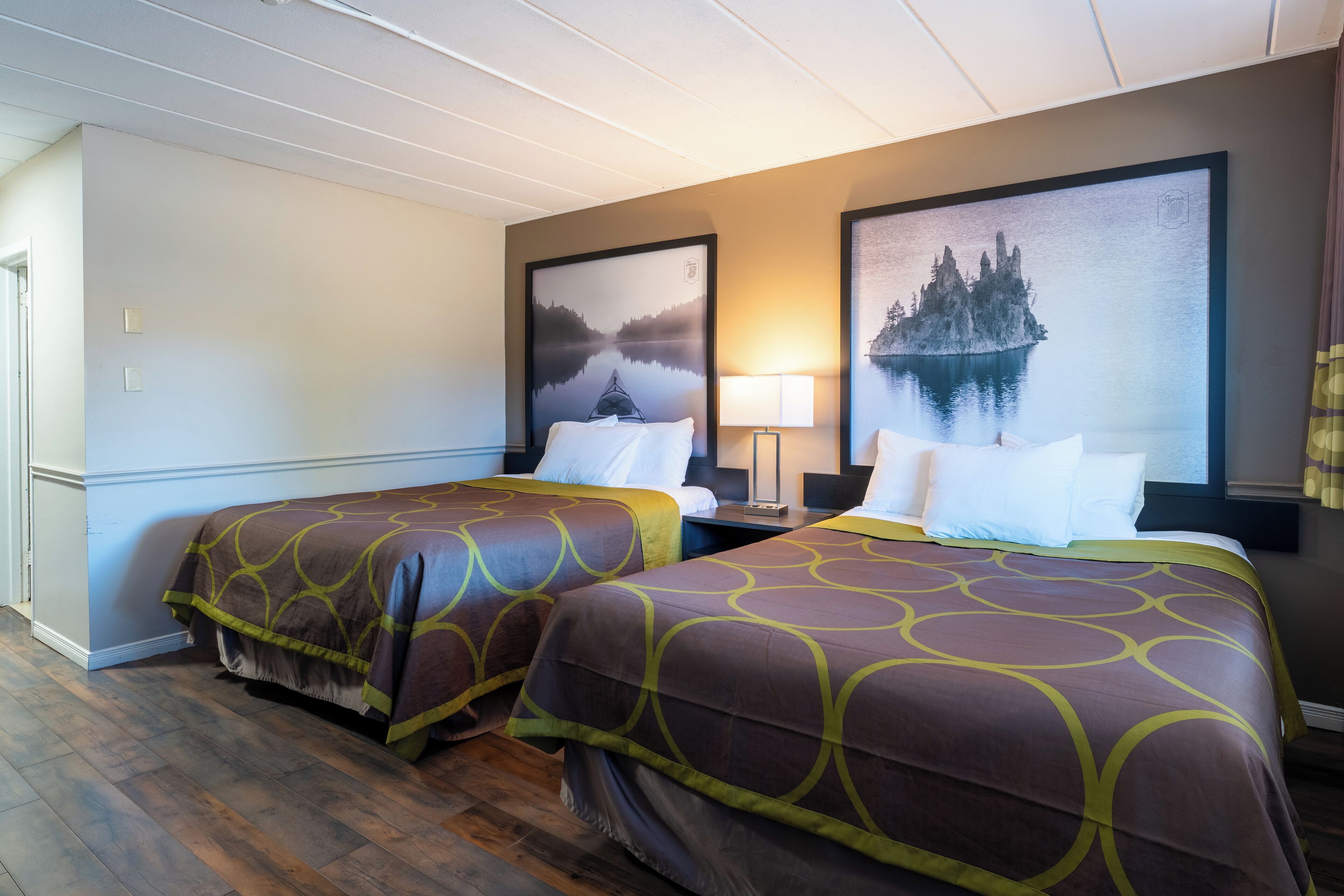 Une chambre d’hôtel avec deux lits, une table de chevet, une lampe et deux tableaux encadrés au mur.