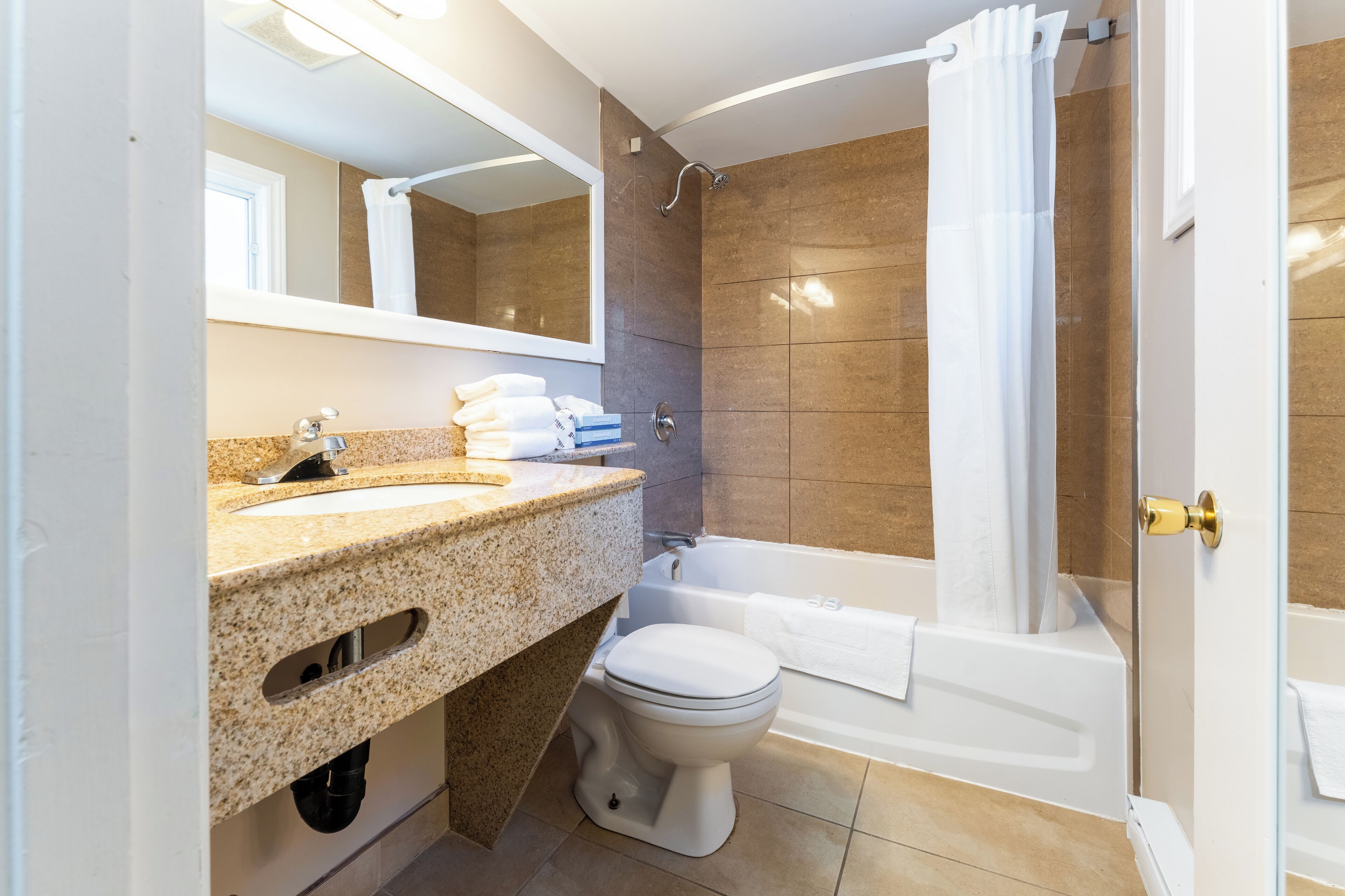 Een moderne badkamer met een wastafel met granieten blad, een toilet, een badkuip en een douche met glazen deur.