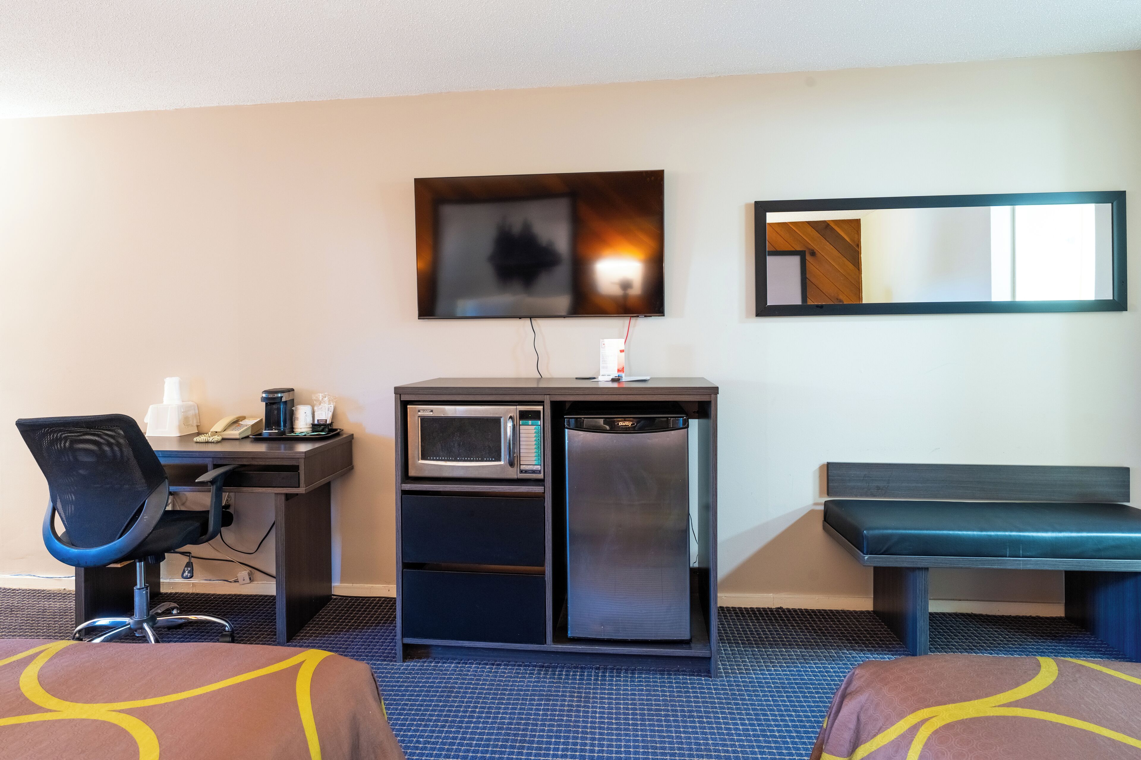 A hotel room with a desk, microwave, refrigerator, and a bench.