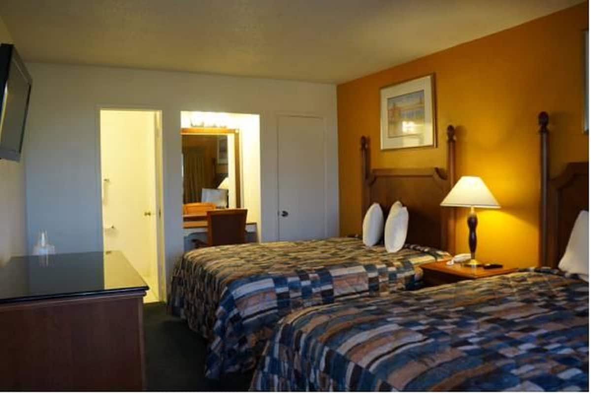 A hotel room with two beds, a desk, a chair, a lamp, and a painting on the wall.