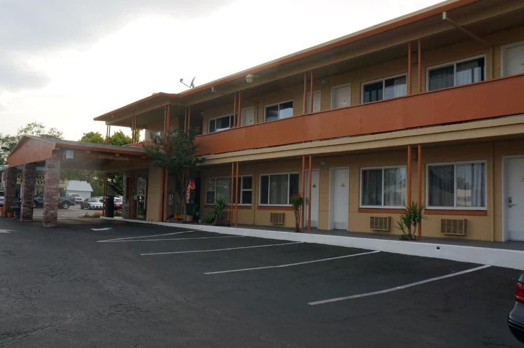 A multi-story motel with a covered entrance, a parking lot, and a row of rooms with windows.