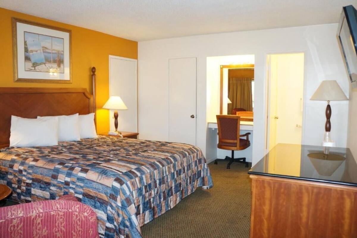 A hotel room with a bed, desk, chair, and a mirror.