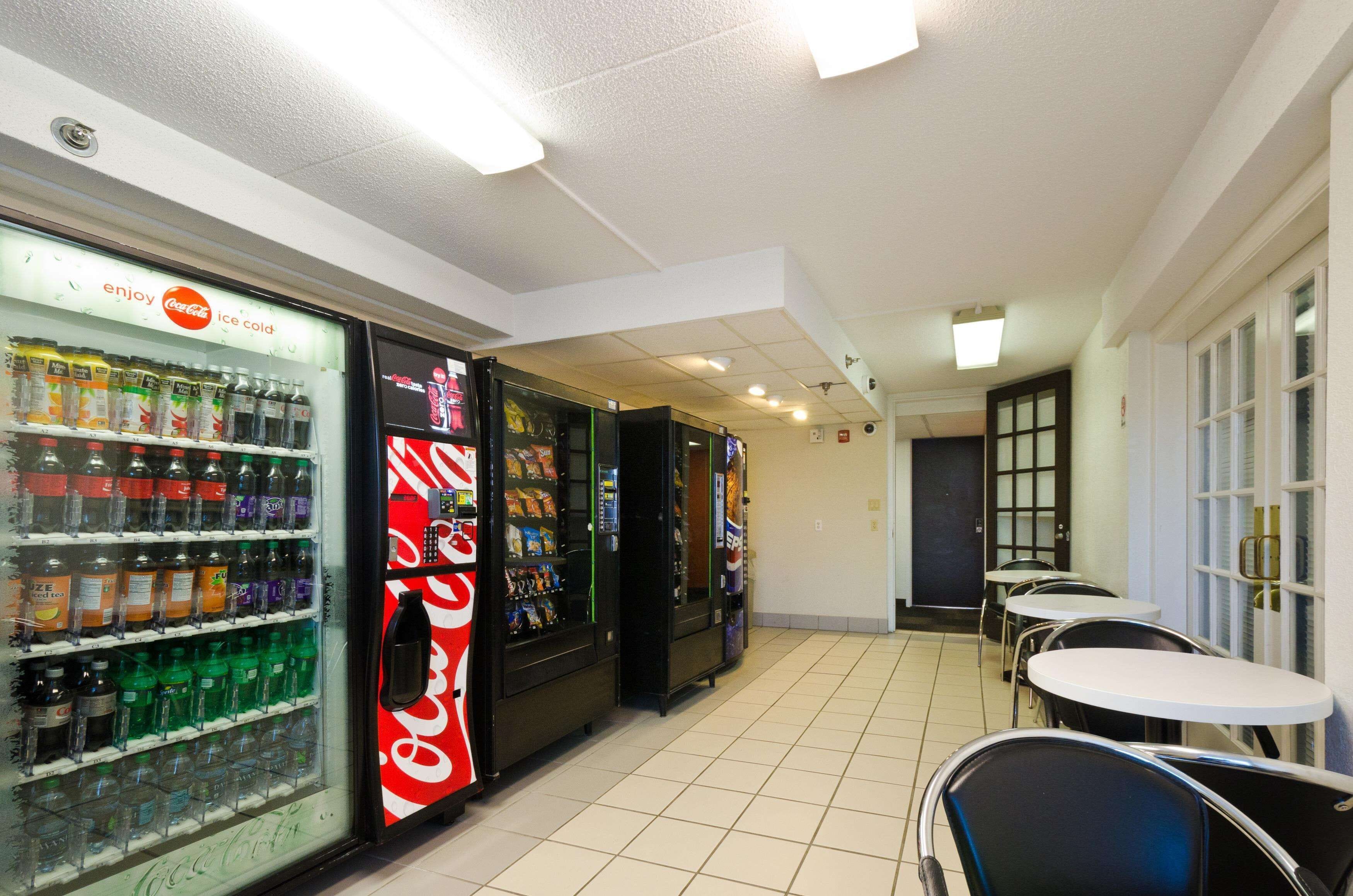 A vending area with various drink options, including Coca-Cola and other beverages. There are tables and chairs for seating.