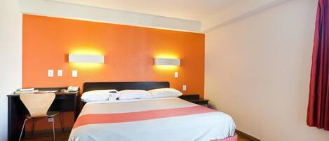 Una habitación de hotel con cama, escritorio, silla y dos lámparas de pared.