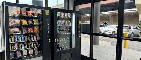 A vending machine area with snacks and drinks, a push-to-open emergency exit door, and a view of parked cars outside.