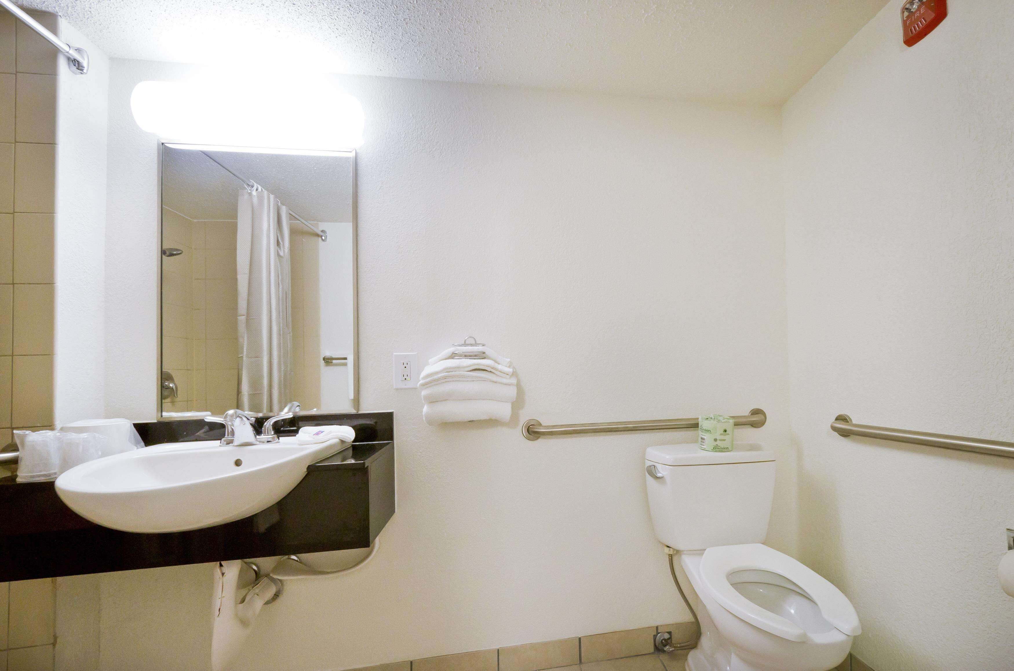 A bathroom with a sink, toilet, and handrails.