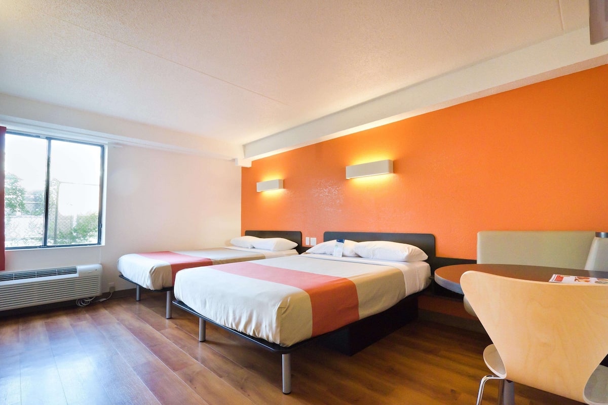Une chambre d’hôtel avec deux lits, un plancher en bois, une fenêtre et une table avec des chaises.