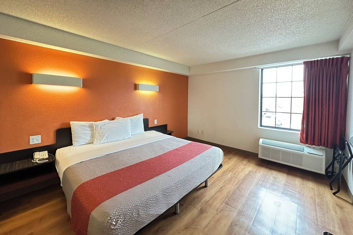 Une chambre d’hôtel avec un lit, deux lampes fixées au mur, une fenêtre avec des rideaux et un radiateur.