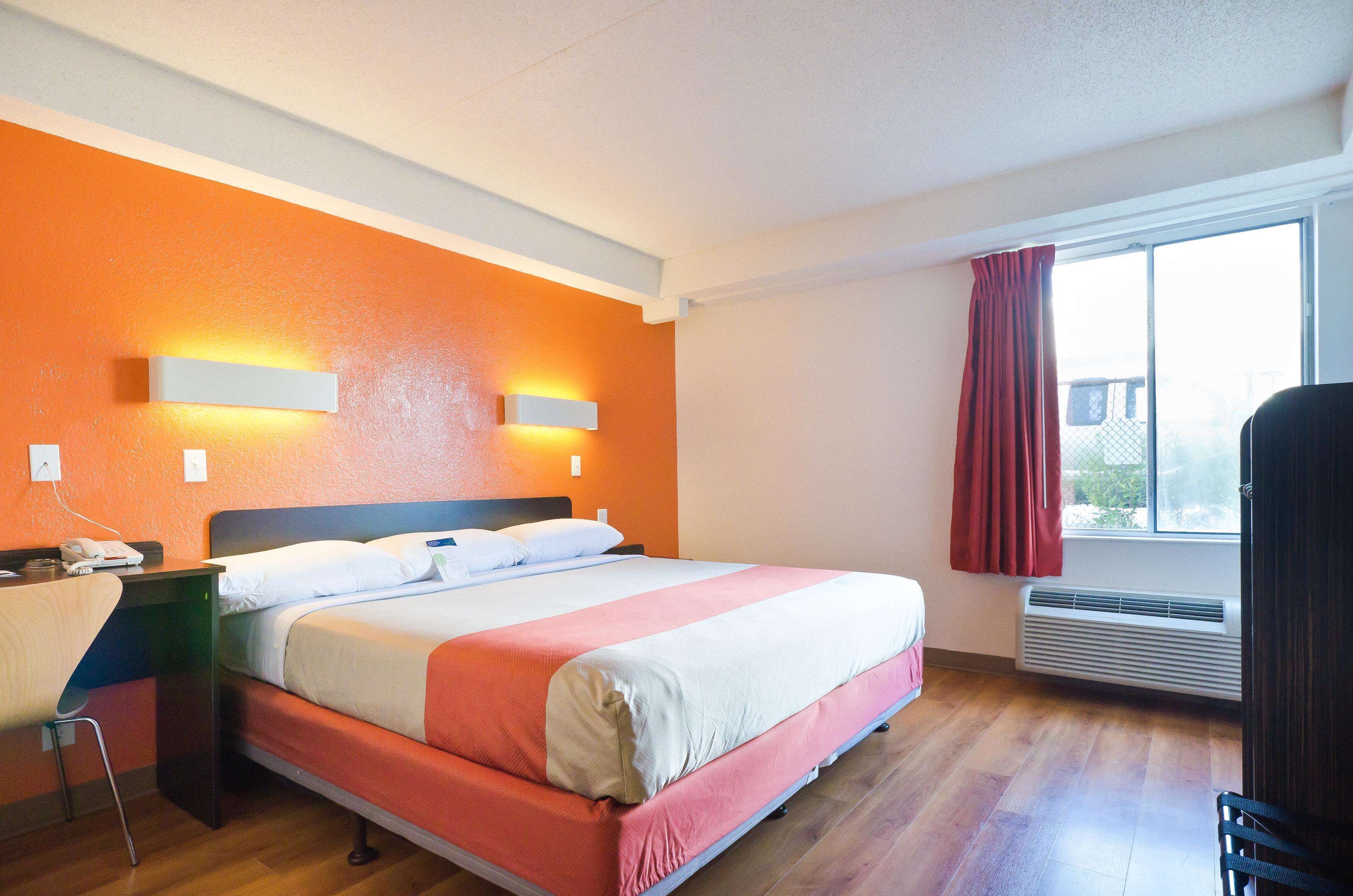 A hotel room with a bed, a desk, a chair, a window with a view, and an air conditioning unit.