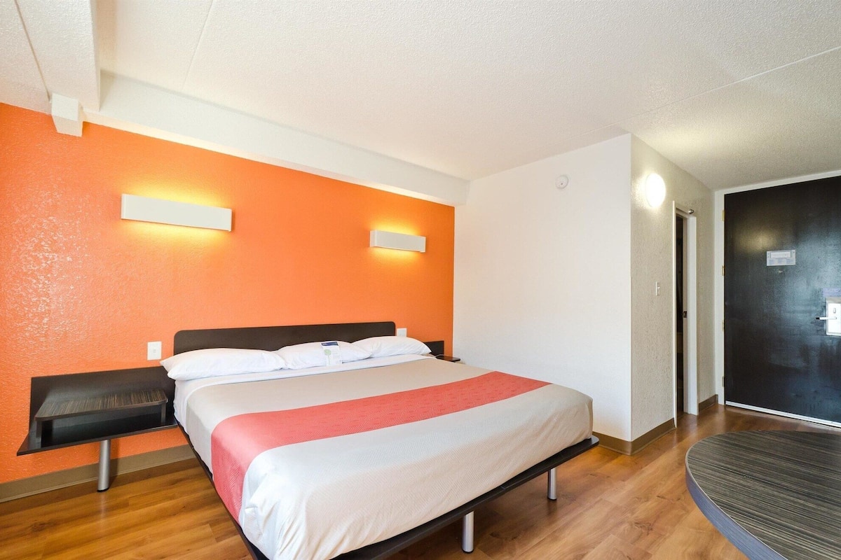 Une chambre d’hôtel avec un lit, des tables de chevet, un bureau et une porte.