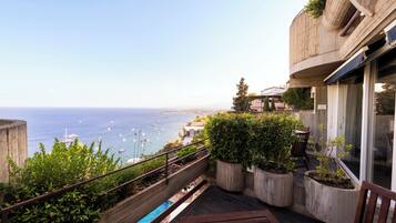 A balcony with a view of the sea, potted plants, and a wooden bench.