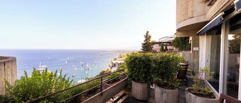 A balcony with a view of the sea, potted plants, and a wooden bench.