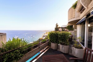 Un balcón con vista al mar, plantas en macetas y un banco de madera.