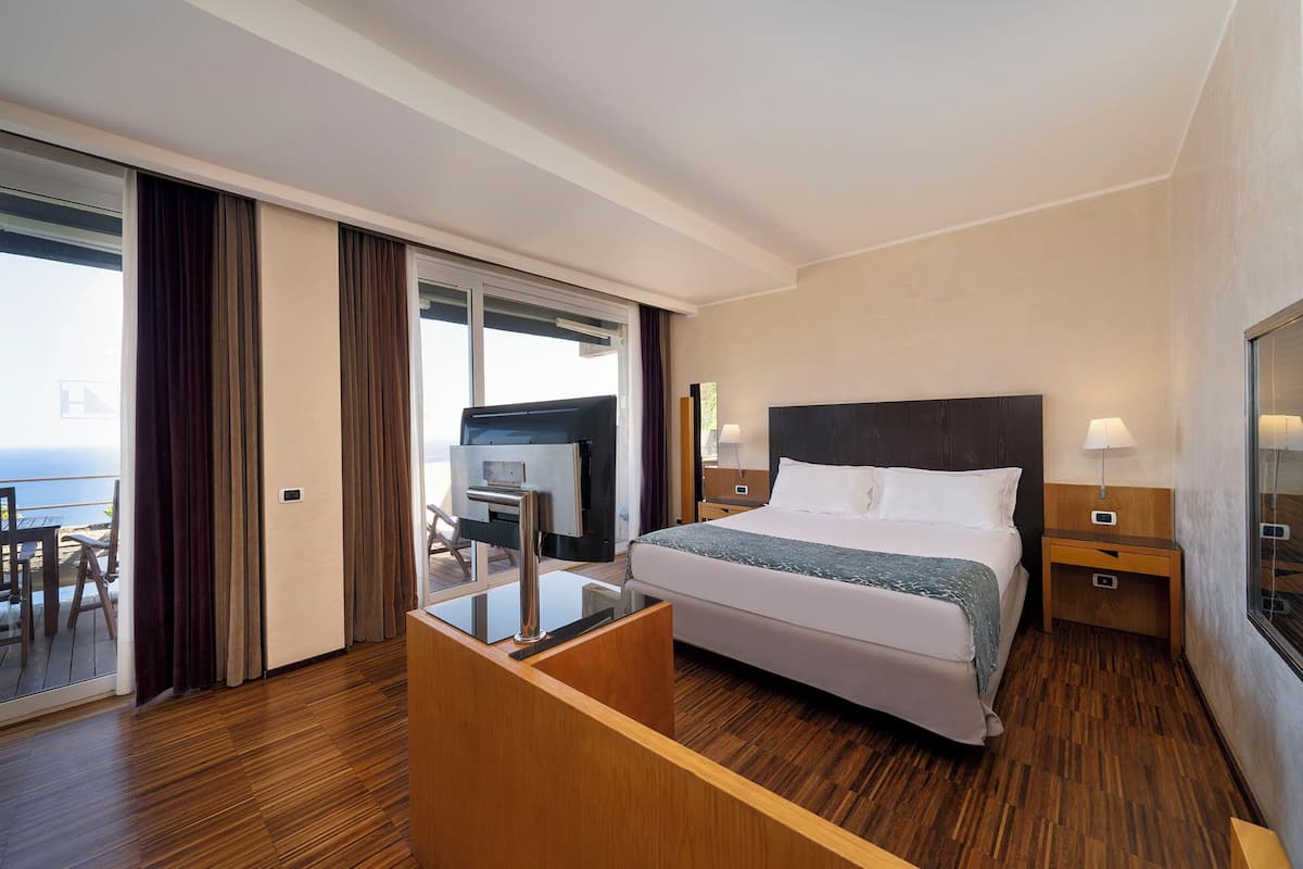 Un cuarto de hotel con cama, mesitas de noche, un escritorio y vista al océano.
