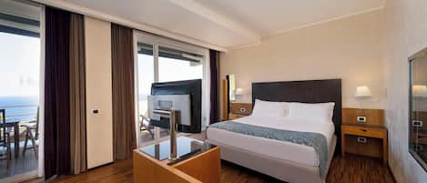 Un cuarto de hotel con cama, mesitas de noche, un escritorio y vista al océano.