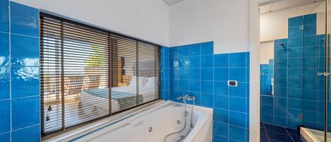 A bathroom with a bathtub, blue tiles, and a window with blinds.