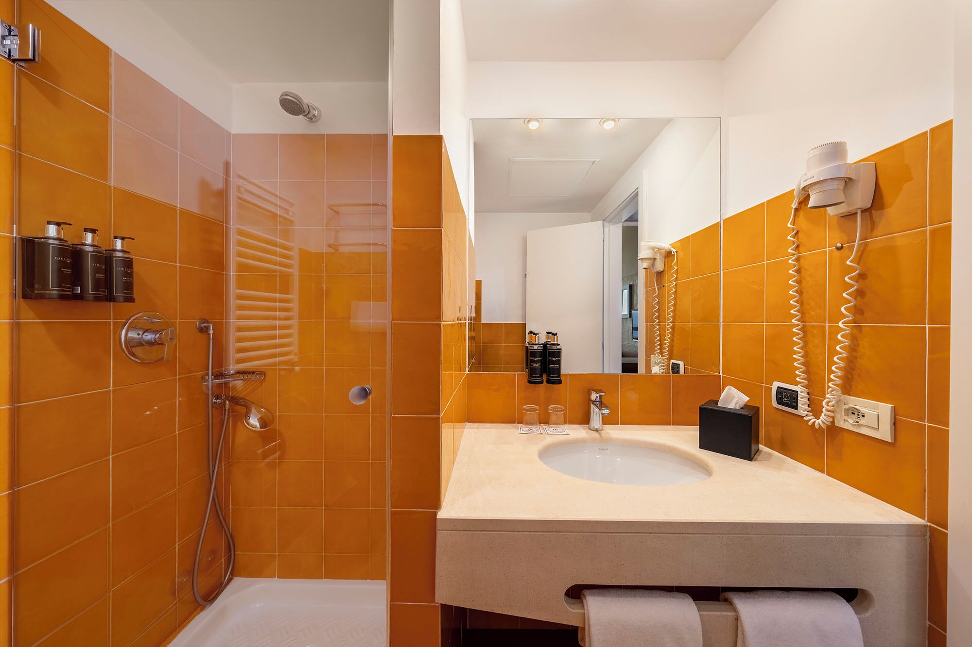 Une salle de bain moderne avec des carreaux orange, une douche, un lavabo et un miroir.