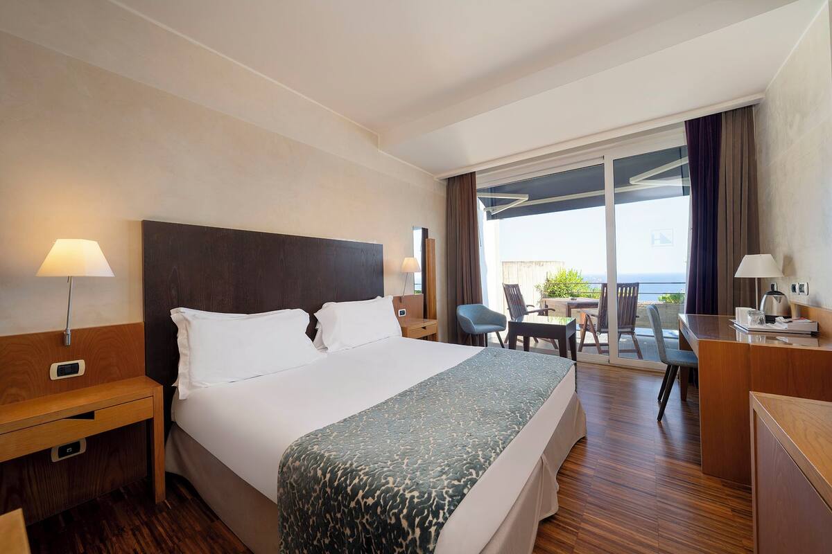 Habitación de hotel con una cama grande, un escritorio, una silla y un balcón con vistas.