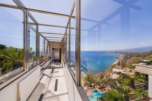 A high-rise building with a glass corridor leading to a balcony with a pool and ocean view. - Eurostars Monte Tauro (Taormina)