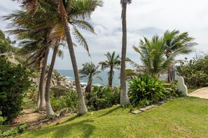 A coastal landscape with palm trees, a grassy area, and a view of the ocean. - Villas Fa-Sol (Santa María Huatulco)