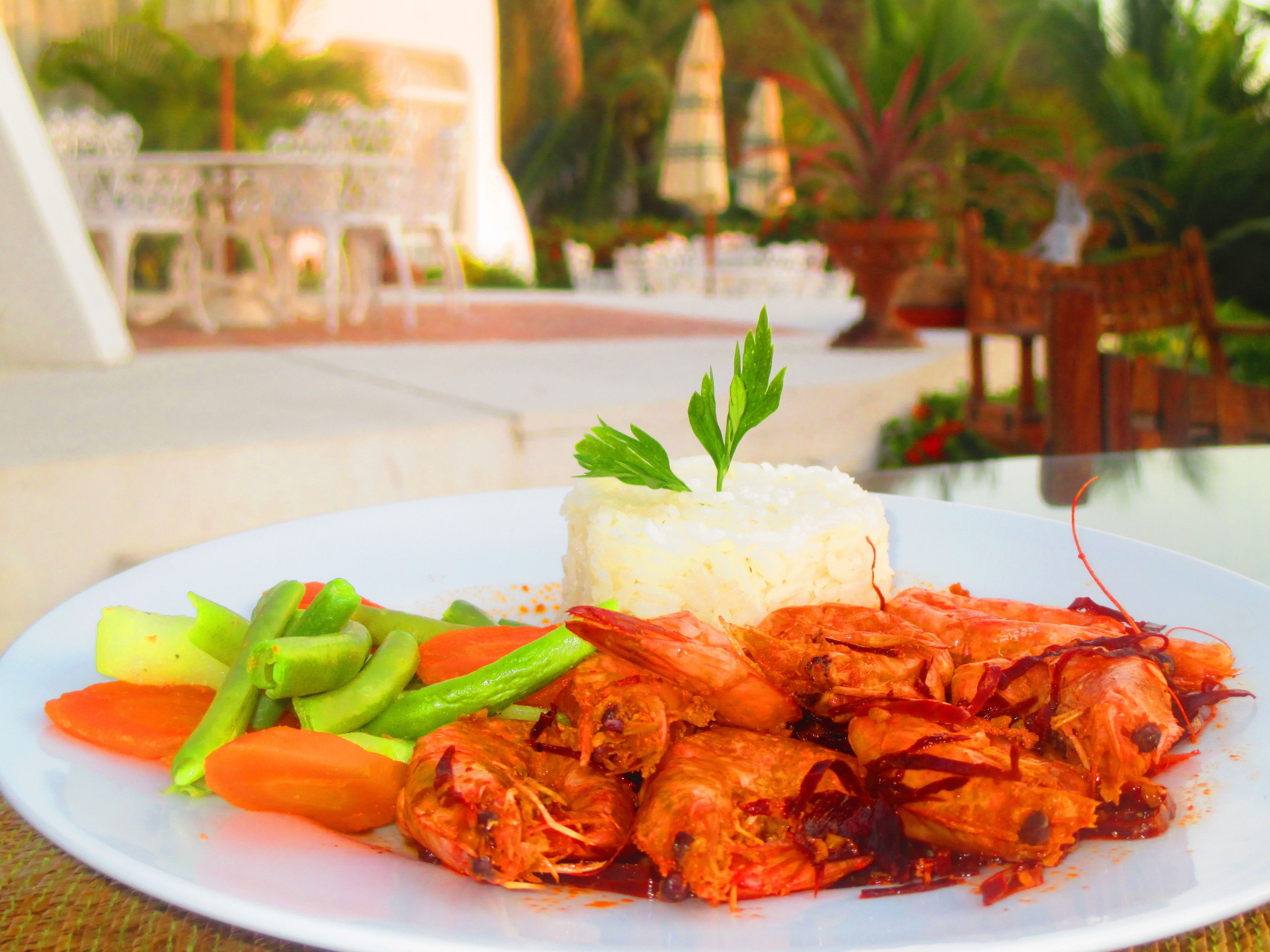 A plate of food with rice, shrimp, and vegetables on a table outdoors.