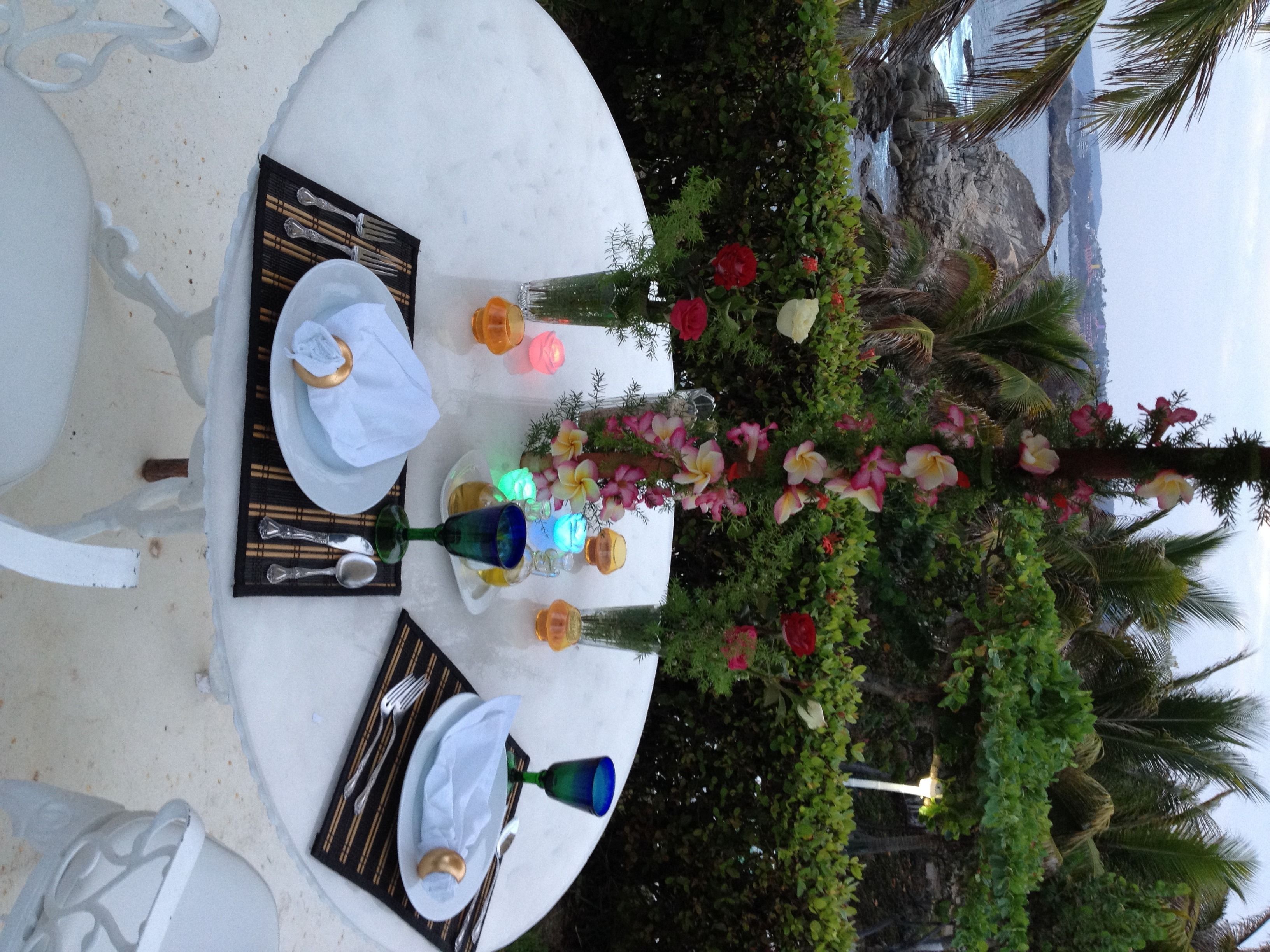 Una mesa lista para una comida, con vistas a una costa rocosa y palmeras.