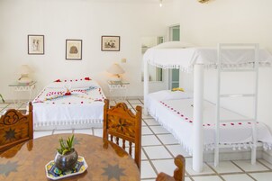 Una habitación de hotel con una cama, una litera, una mesa de comedor con sillas, un florero con flores y dos mesitas de noche con lámparas.