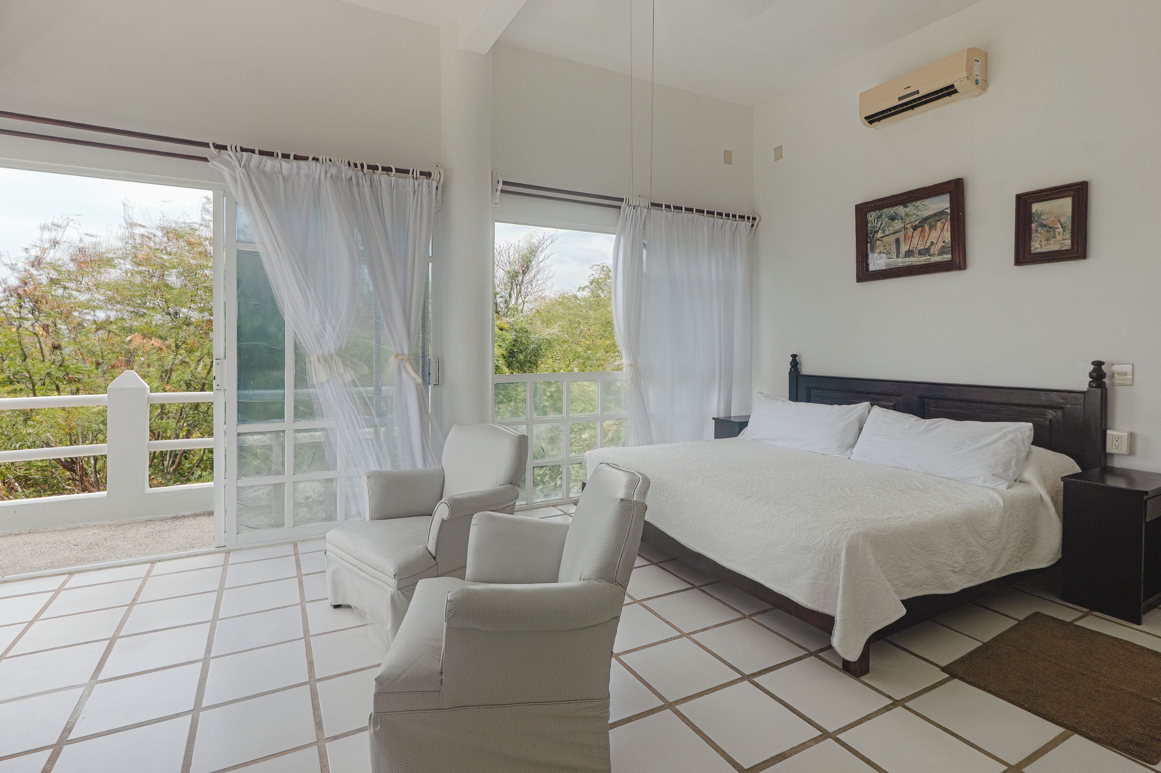 A bedroom with a bed, two chairs, a nightstand, and a balcony with curtains.