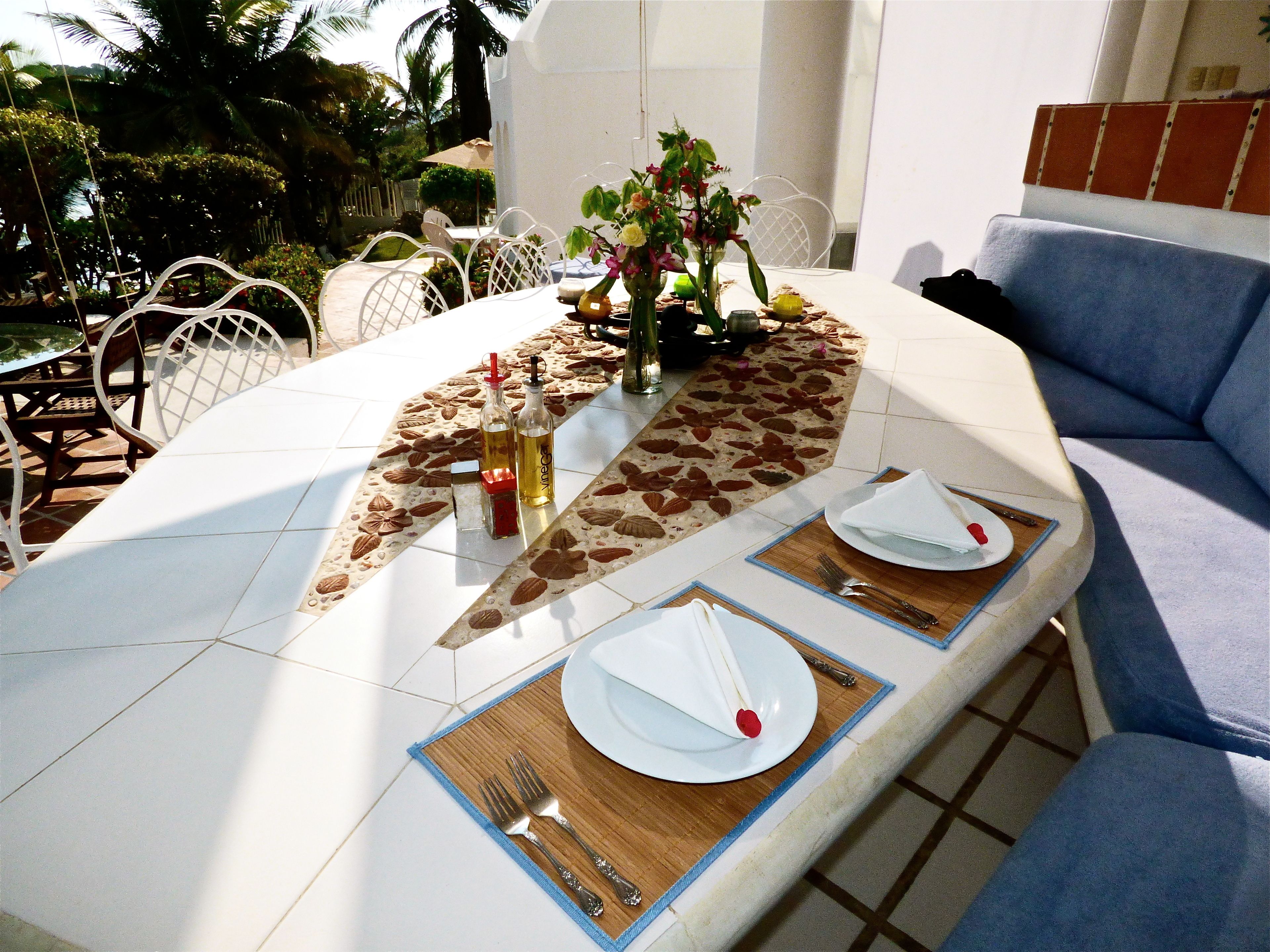 A dining table set for two with a tropical leaf-patterned table runner, white plates, and cutlery.