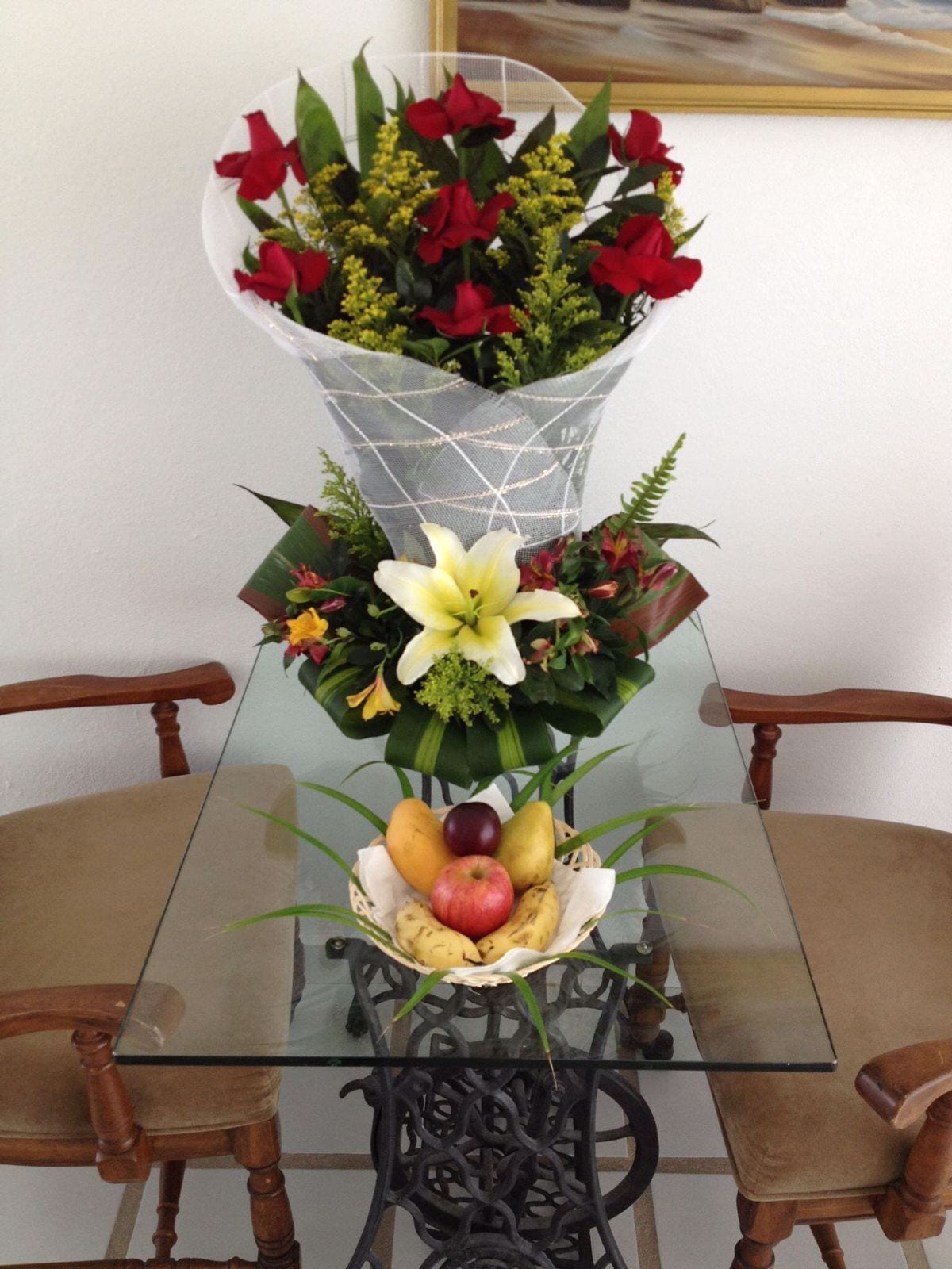 Una mesa de cristal con un arreglo floral y una cesta de frutas.