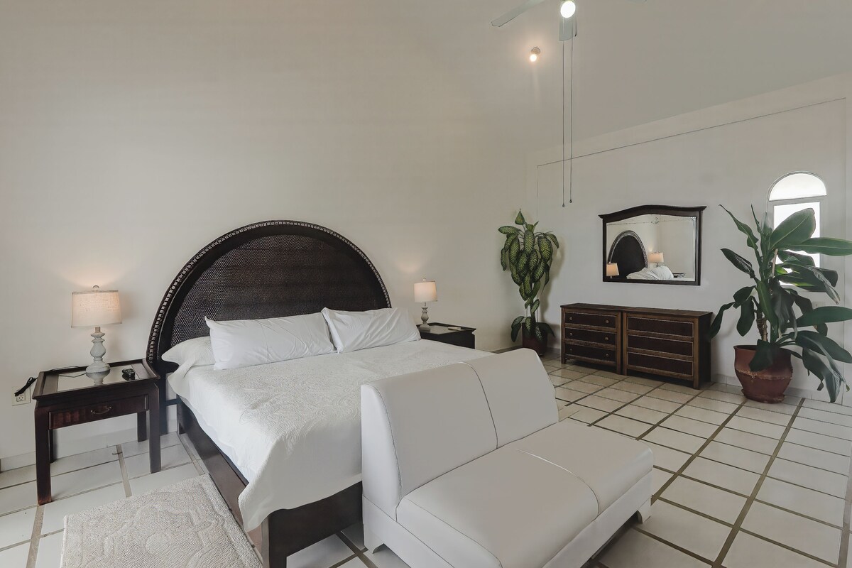 A bedroom with a bed, a nightstand, a dresser, a potted plant, and a mirror.