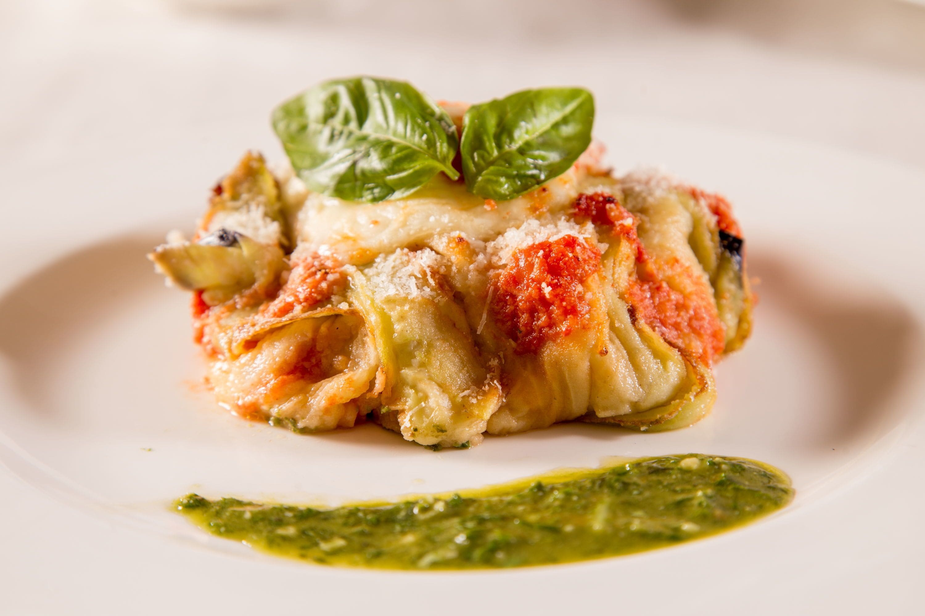 A plate of ravioli with a basil leaf garnish and a green sauce.