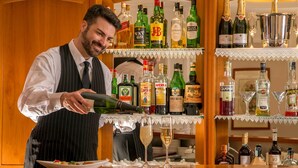 Um bartender a servir uma bebida num bar com estantes de garrafas de licor e copos.