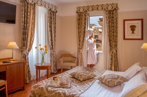A hotel room with a bed, a desk, a chair, a table with flowers, and a breakfast tray.
