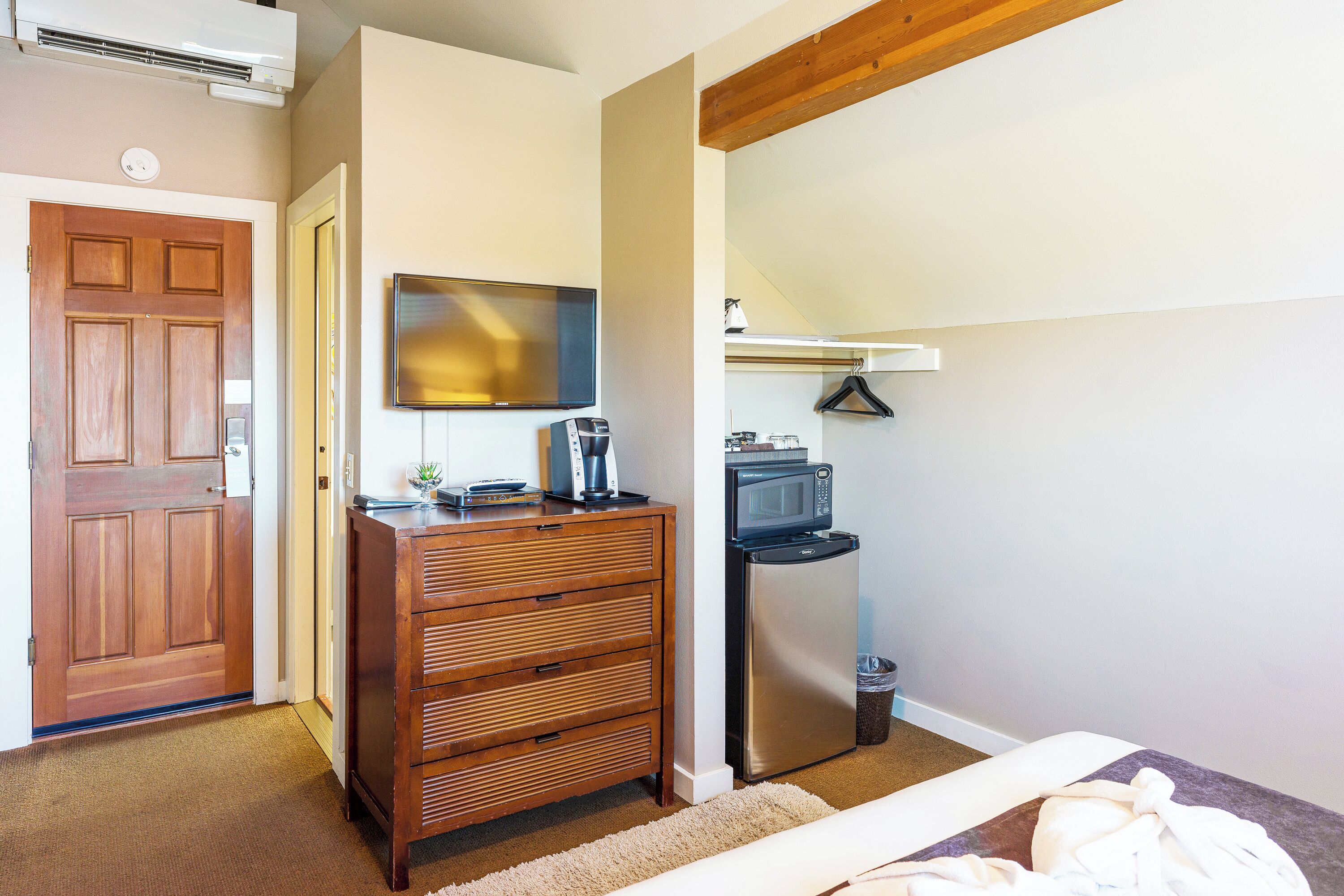 A bedroom with a wooden dresser, a flat-screen TV, a microwave, and a refrigerator.