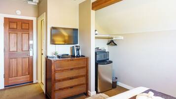 A bedroom with a wooden dresser, a flat-screen TV, a microwave, and a refrigerator.