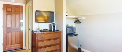 A bedroom with a wooden dresser, a flat-screen TV, a microwave, and a refrigerator.