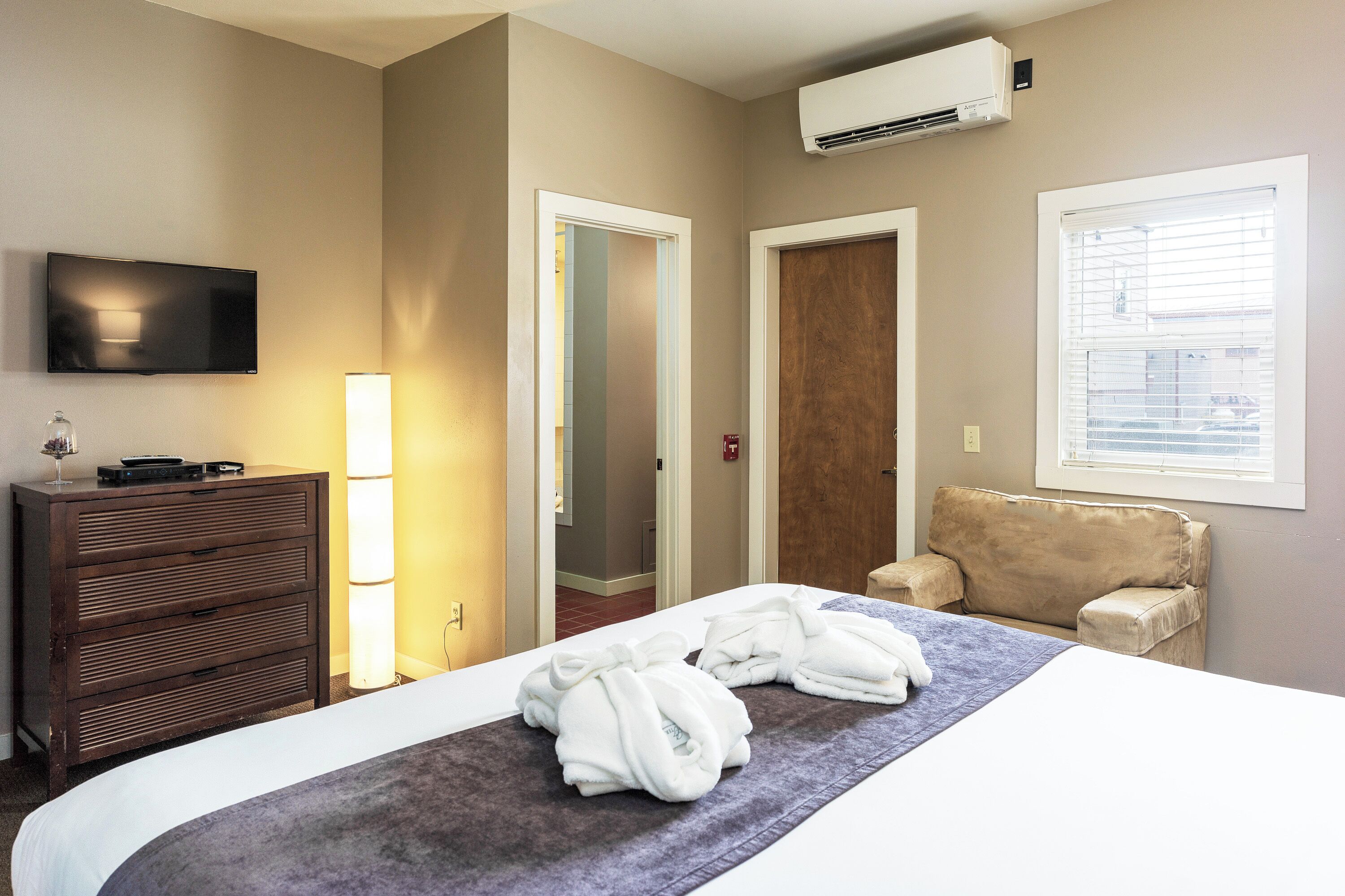 A hotel room with a bed, a TV, a dresser, a chair, and a window.
