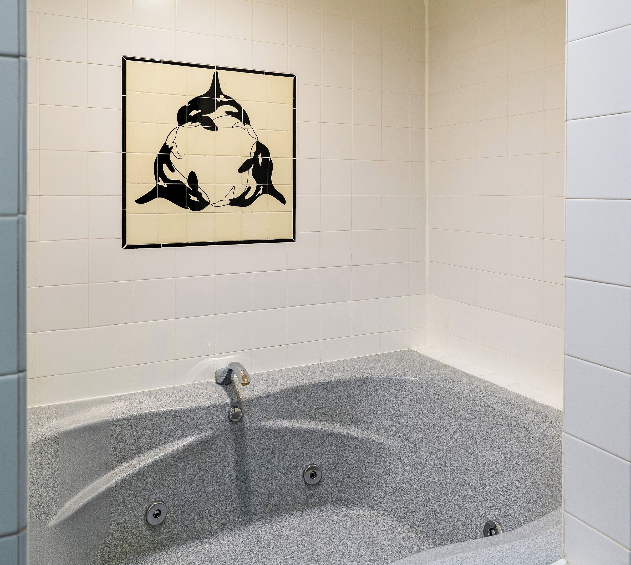 Un baño con bañera, una obra de arte en la pared y paredes cubiertas de azulejos blancos.
